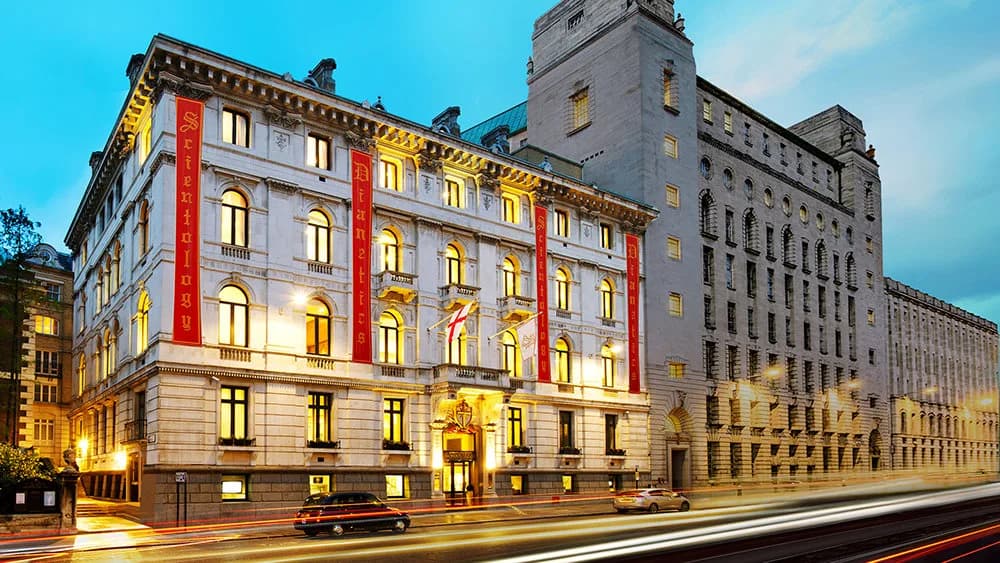 Historic building with pale cream classical stone facade, formal neoclassical architecture, red banners displayed on front, evenly-spaced windows across multiple stories, and grand entrance portico.